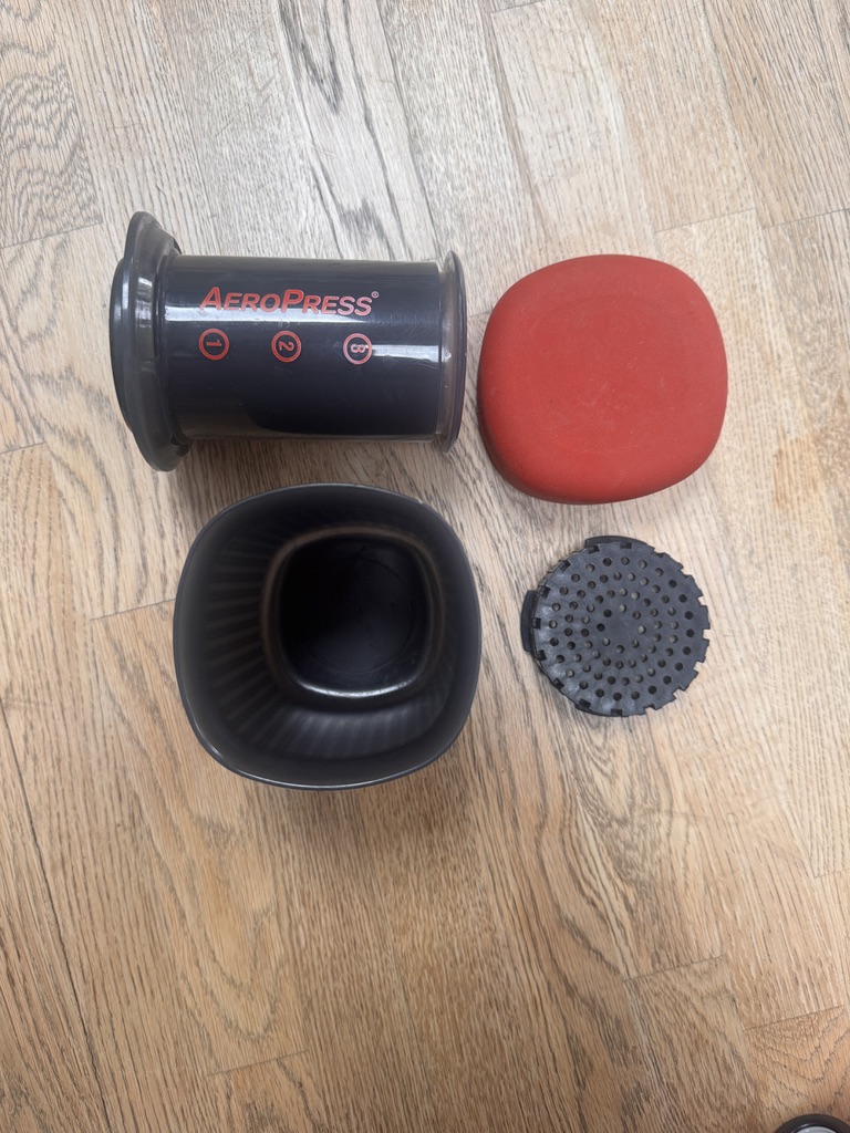 AeroPress Go kit laid out: chamber, plunger, filter cap, mug, and red lid