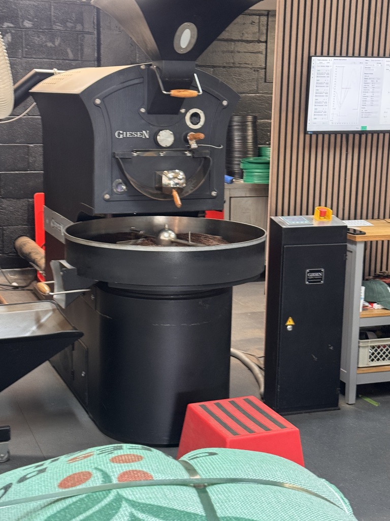 Roast profile monitor on a wooden wall beside a Giesen specialty coffee roaster
